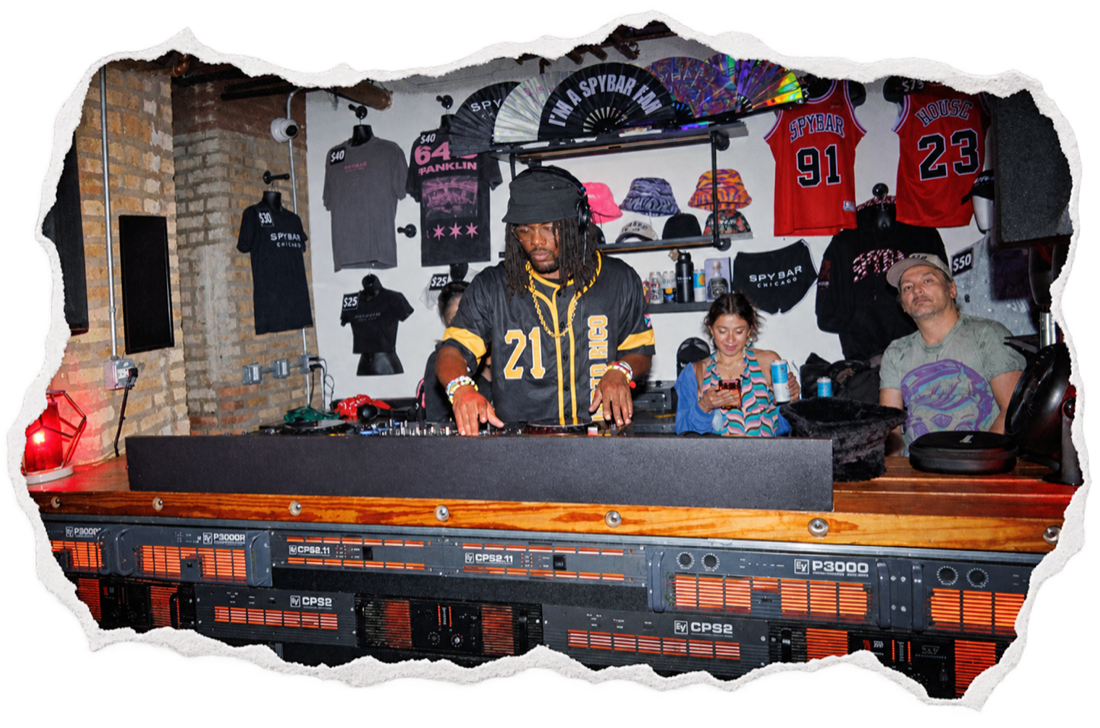 N.Harmonix behind a long DJ booth in front of a wall of jerseys